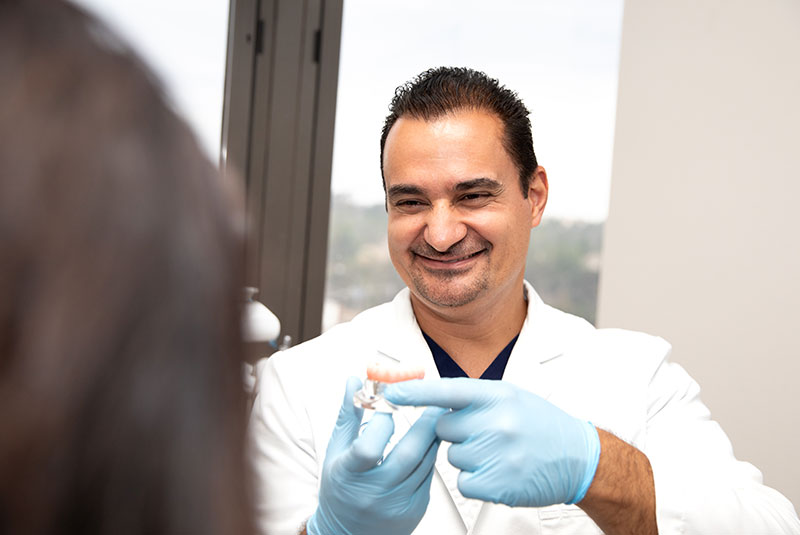 Doctor holding up full arch dental implant for Patient